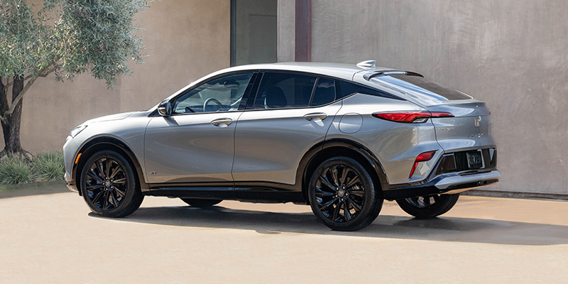 Rear driver's side view of a silver 2025 Buick Envista parked in a residential driveway on a sunny day